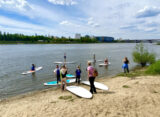 Grupa osób z deskami SUP na piaszczystej plaży nad Wisłą w Warszawie — zajęcia Stand Up Paddle w Dzielnicy Wisła