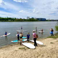 Grupa osób z deskami SUP na piaszczystej plaży nad Wisłą w Warszawie — zajęcia Stand Up Paddle w Dzielnicy Wisła