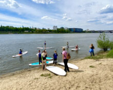 Grupa osób z deskami SUP na piaszczystej plaży nad Wisłą w Warszawie — zajęcia Stand Up Paddle w Dzielnicy Wisła