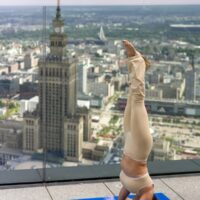 Uczestniczka wykonuje pozycję jogi na tarasie widokowym Varso Tower w Warszawie. W tle widoczny Pałac Kultury i Nauki oraz panorama centrum stolicy.