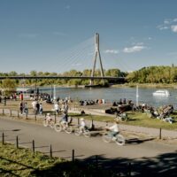 Spacerowicze i rowerzysta na terenach zielonych nad Wisłą