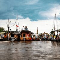 Tradycyjne drewniane łodzie i barki zacumowane obok siebie na Wiśle, z uczestnikami na pokładach